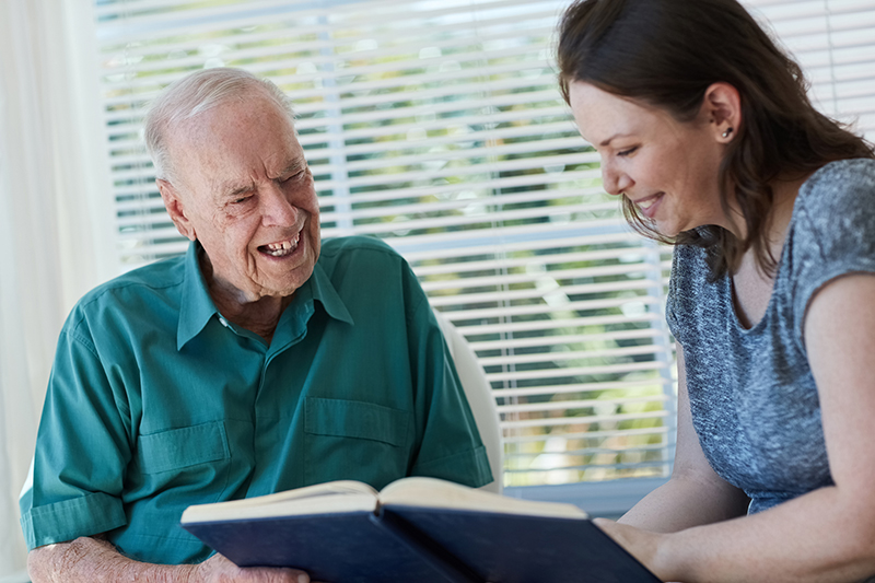 senior man and caregiver looking at book